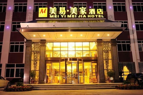The exterior of MEI YI MEI JIA HOTEL with a prominent entrance, large glass doors, and a well-lit facade.