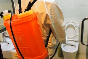 Una persona con ropa de protección limpiando un inodoro con un recipiente naranja.