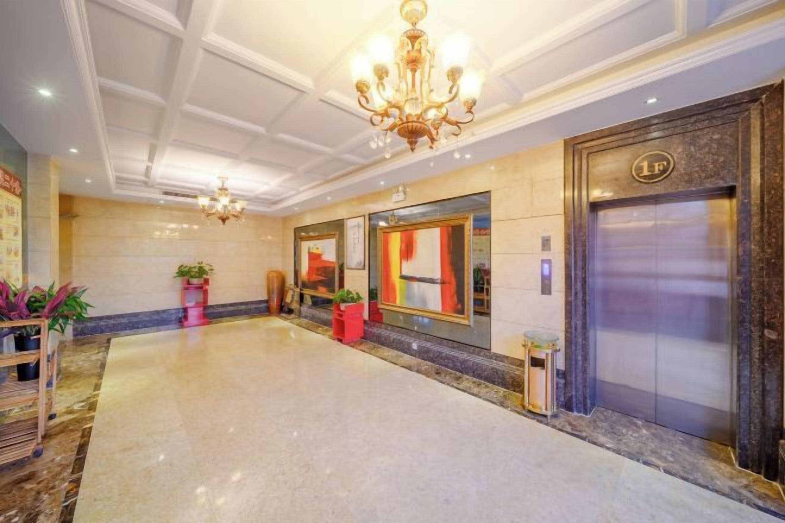 Un vestíbulo de hotel con piso de mármol, un candelabro, un ascensor y plantas en macetas.