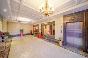 Un vestíbulo de hotel con piso de mármol, un candelabro, un ascensor y plantas en macetas.
