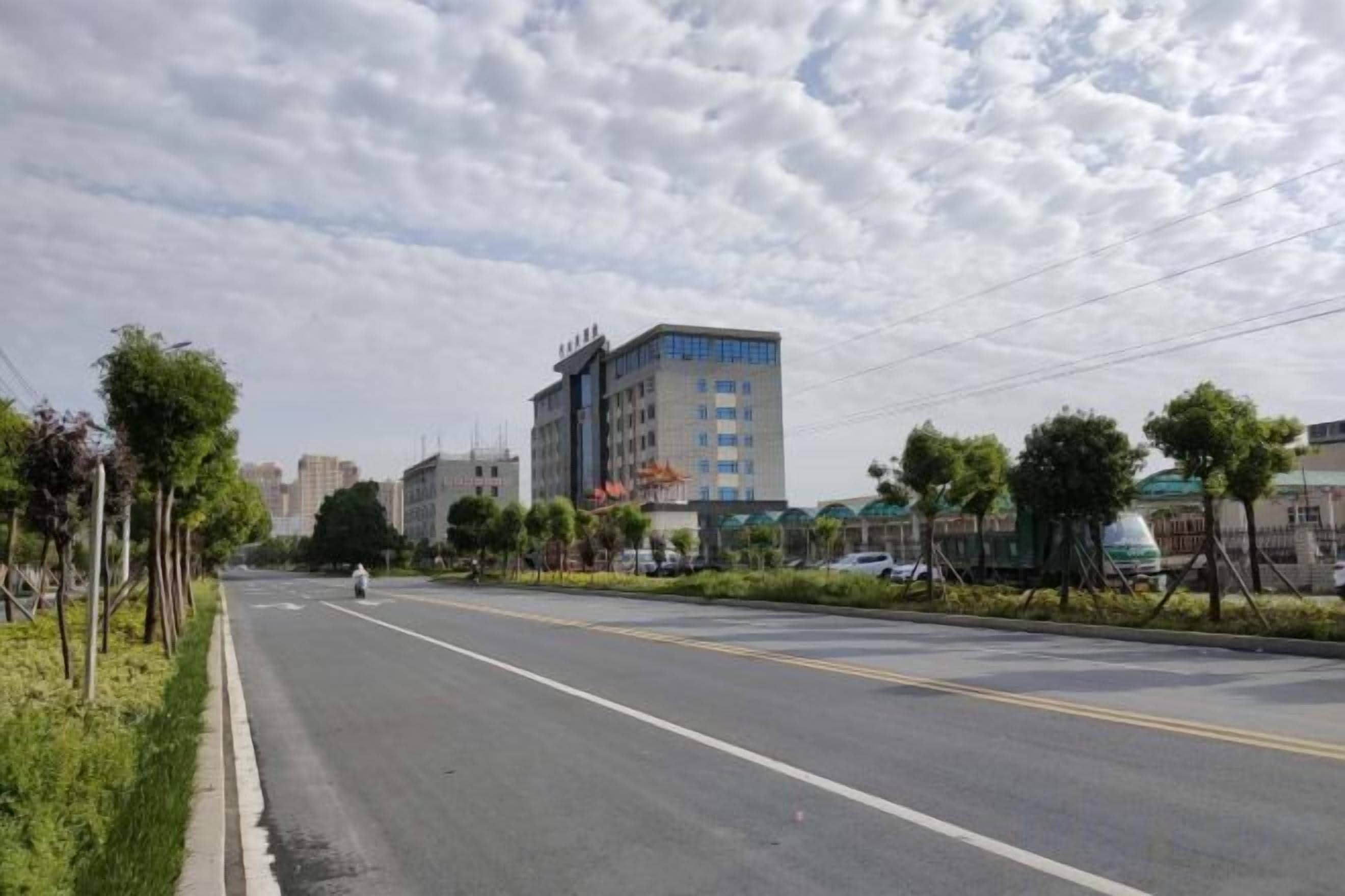 A wide urban road with buildings on both sides, a clear sky, and a few trees along the sidewalk.