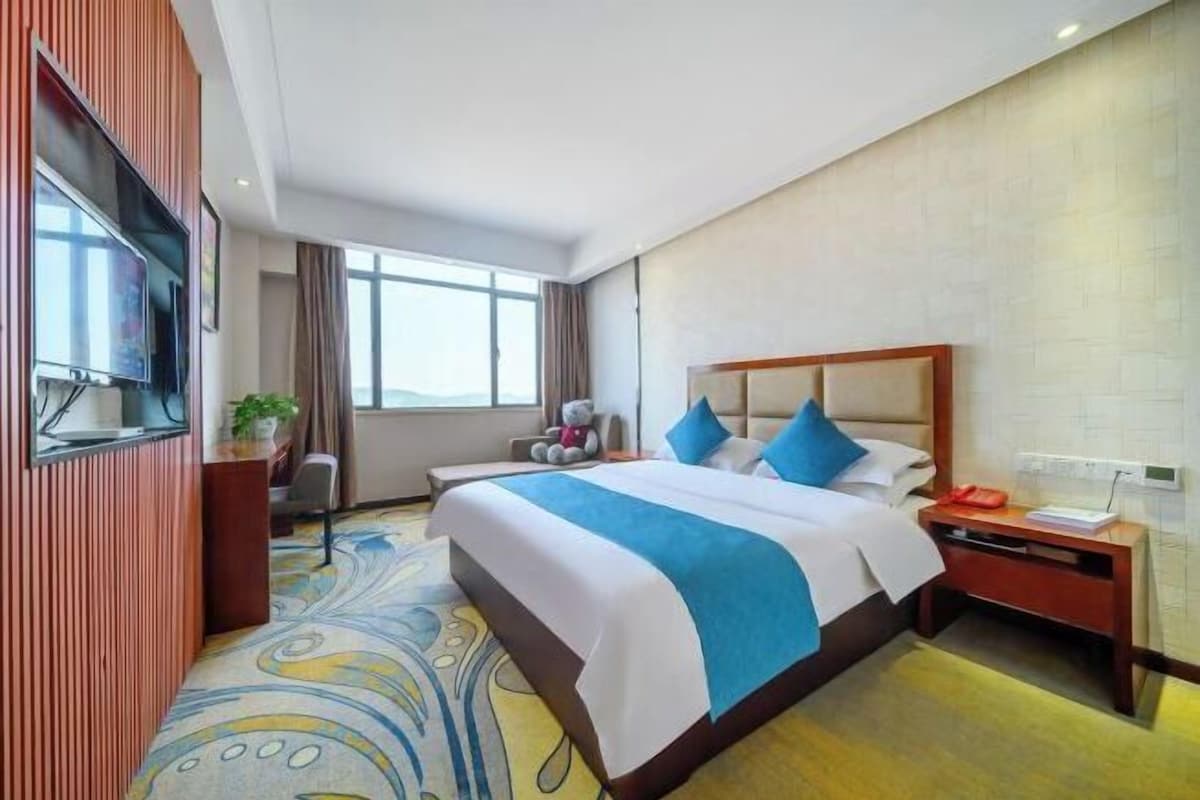 A hotel room with a large bed, a television, a desk, and a view of the outdoors.