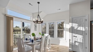 Espaço de refeições com mesa posta para quatro pessoas, janelas amplas e lustre.