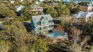 Uma casa grande com piscina, cercada por árvores e outras casas.