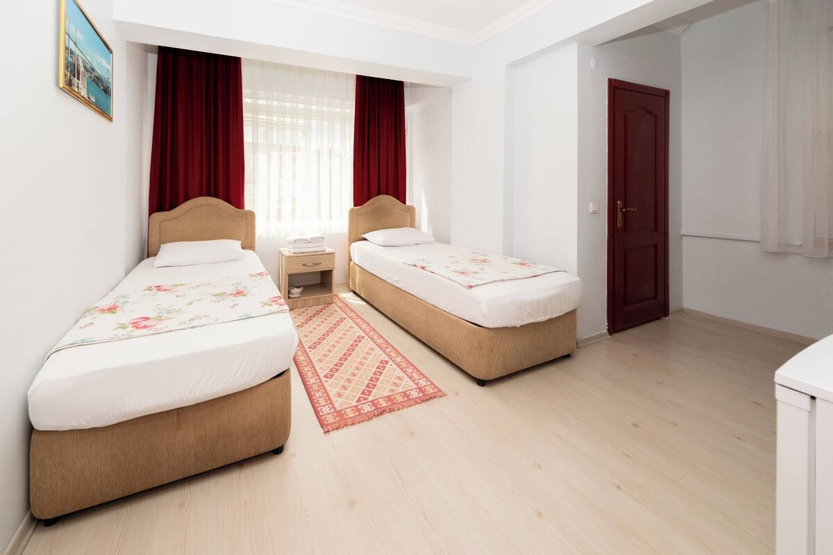 A hotel room with two single beds, a small desk, a red patterned rug, and a door.