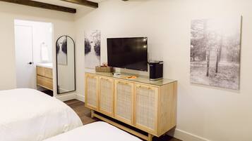 Un dormitorio con una cama, un armario de madera con un televisor, un espejo y dos cuadros colgados en la pared.