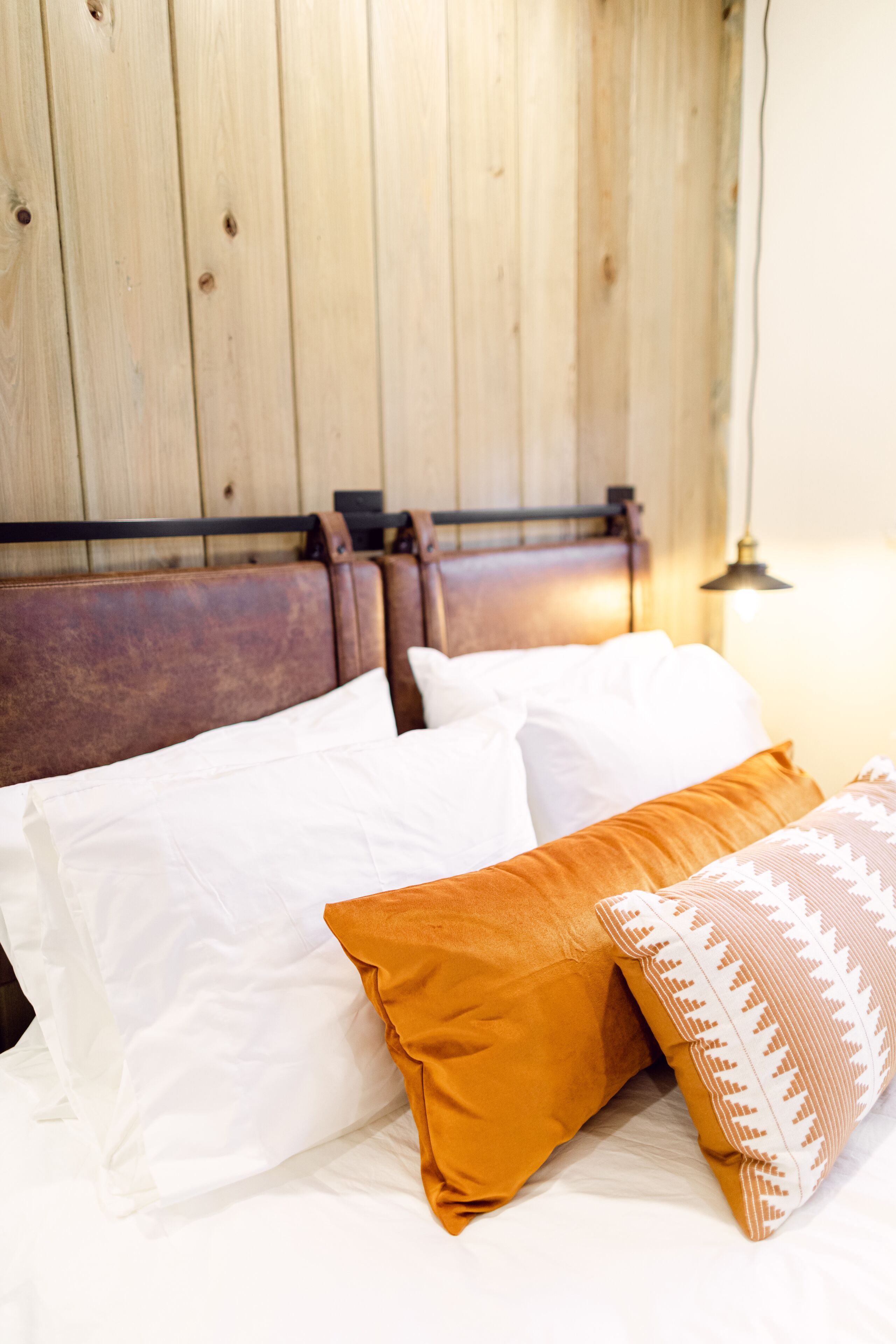 A bed with white and brown pillows, a wooden headboard, and a wall-mounted lamp.