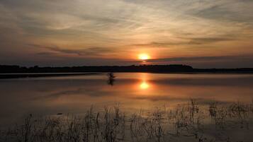 A calm lake at sunset with a clear sky and distant trees.