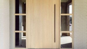 Una puerta de madera con un picaporte vertical, flanqueada por dos ventanas.