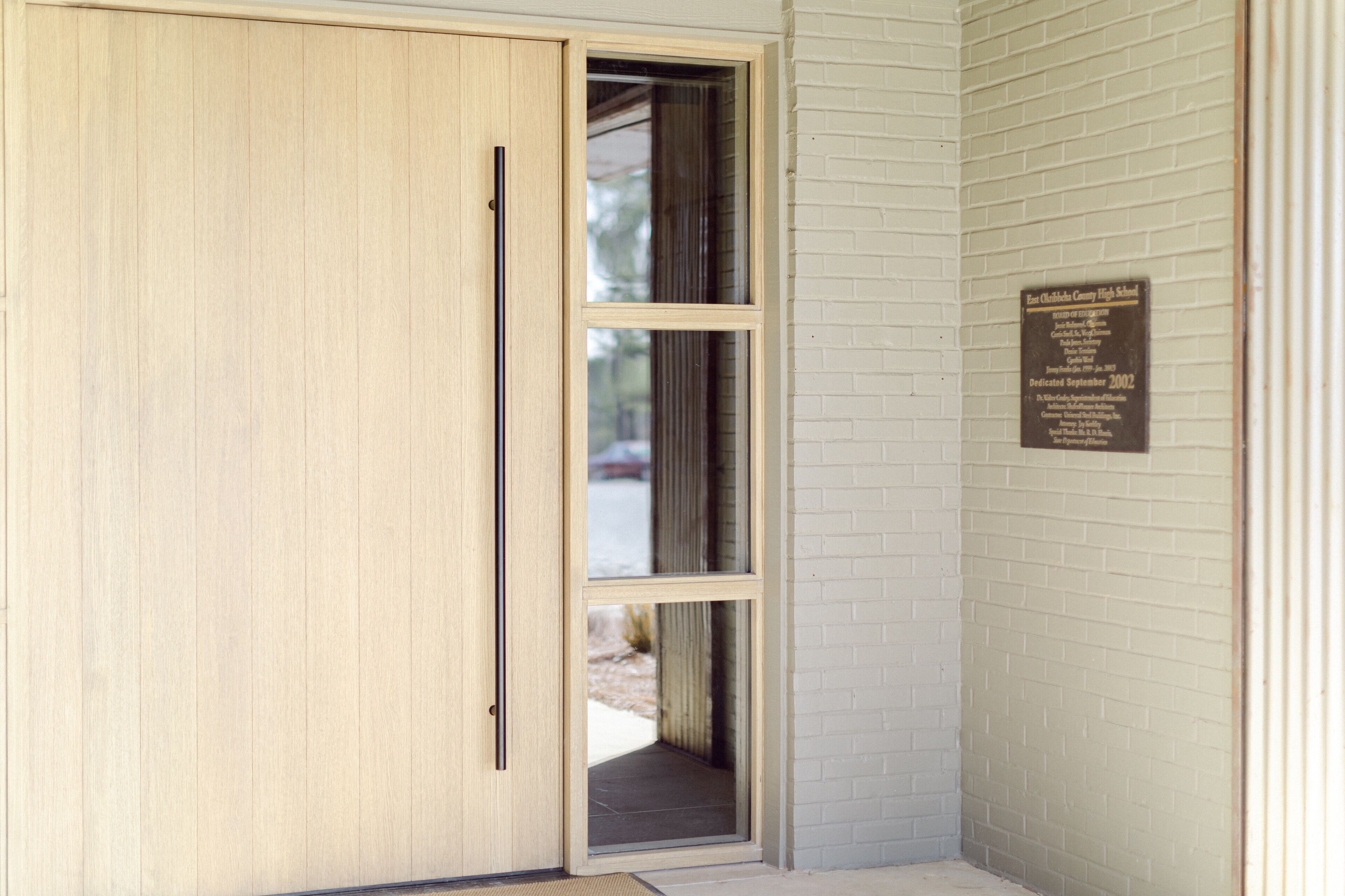 A wooden door with a sliding glass panel, a brick wall, and a plaque on the wall.