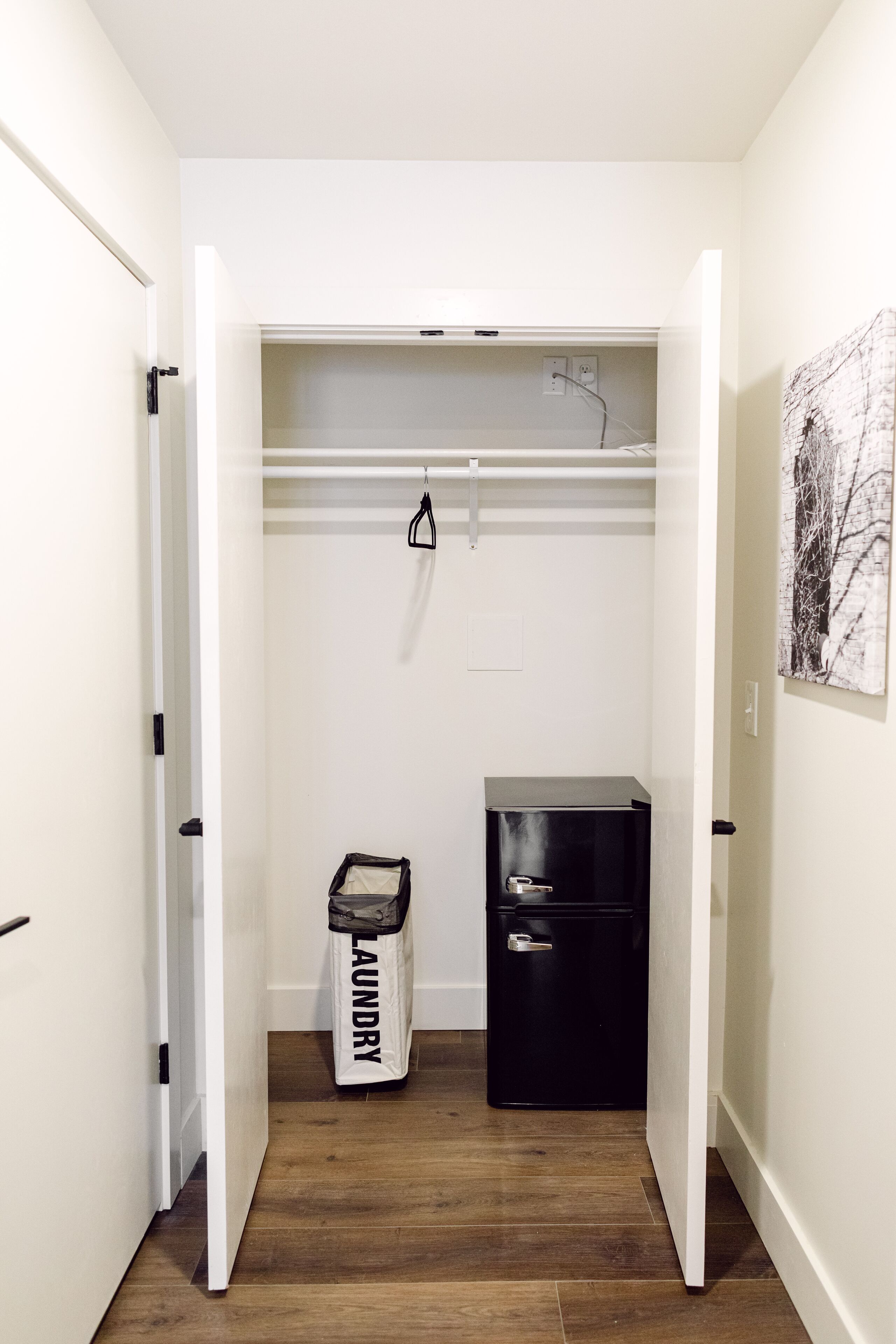 Un pasillo estrecho con un armario blanco, un mueble negro para guardar cosas y una bolsa de lavandería en el suelo.