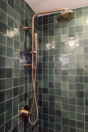 A shower with a curved hose and a handheld showerhead, mounted on a wall with green tiles.