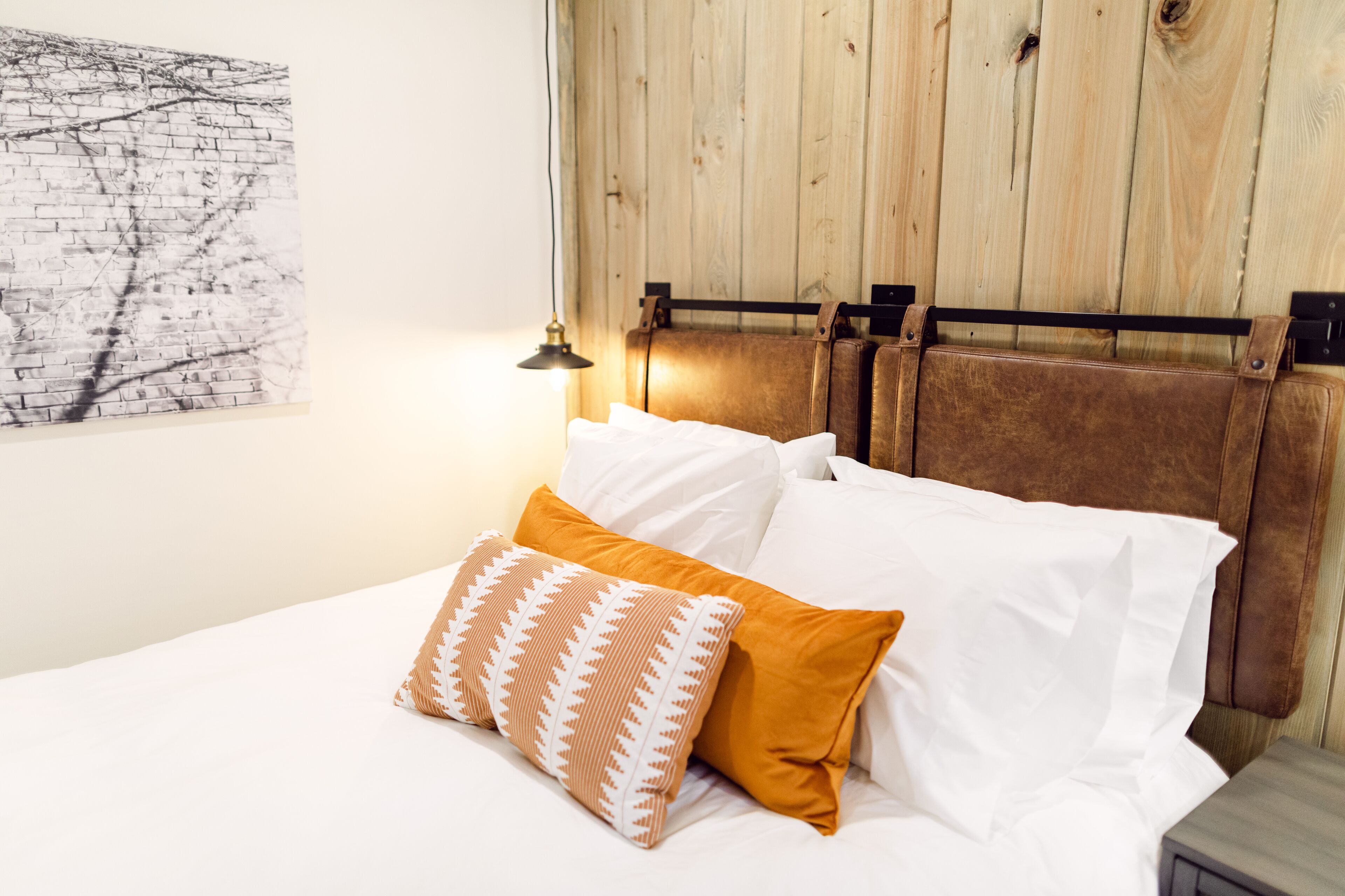 A bed with white and mustard pillows, a wooden headboard, and a wall-mounted lamp.
