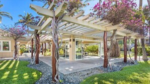 Ein überdachter Außenbereich mit einer Pergola, Bäumen und einem Weg zu einem Gebäude.