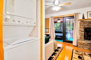 A laundry area with a dryer and a ceiling fan, a living room with a sofa and a fireplace, and a view of the outdoors through a sliding glass door.