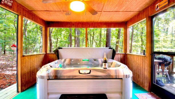 Een hottub in een houten chalet met een plafondventilator, grote ramen en uitzicht op het bos.