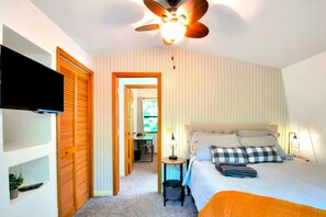 Une chambre à coucher comprenant un lit, un ventilateur de plafond, un téléviseur et un bureau avec une chaise.