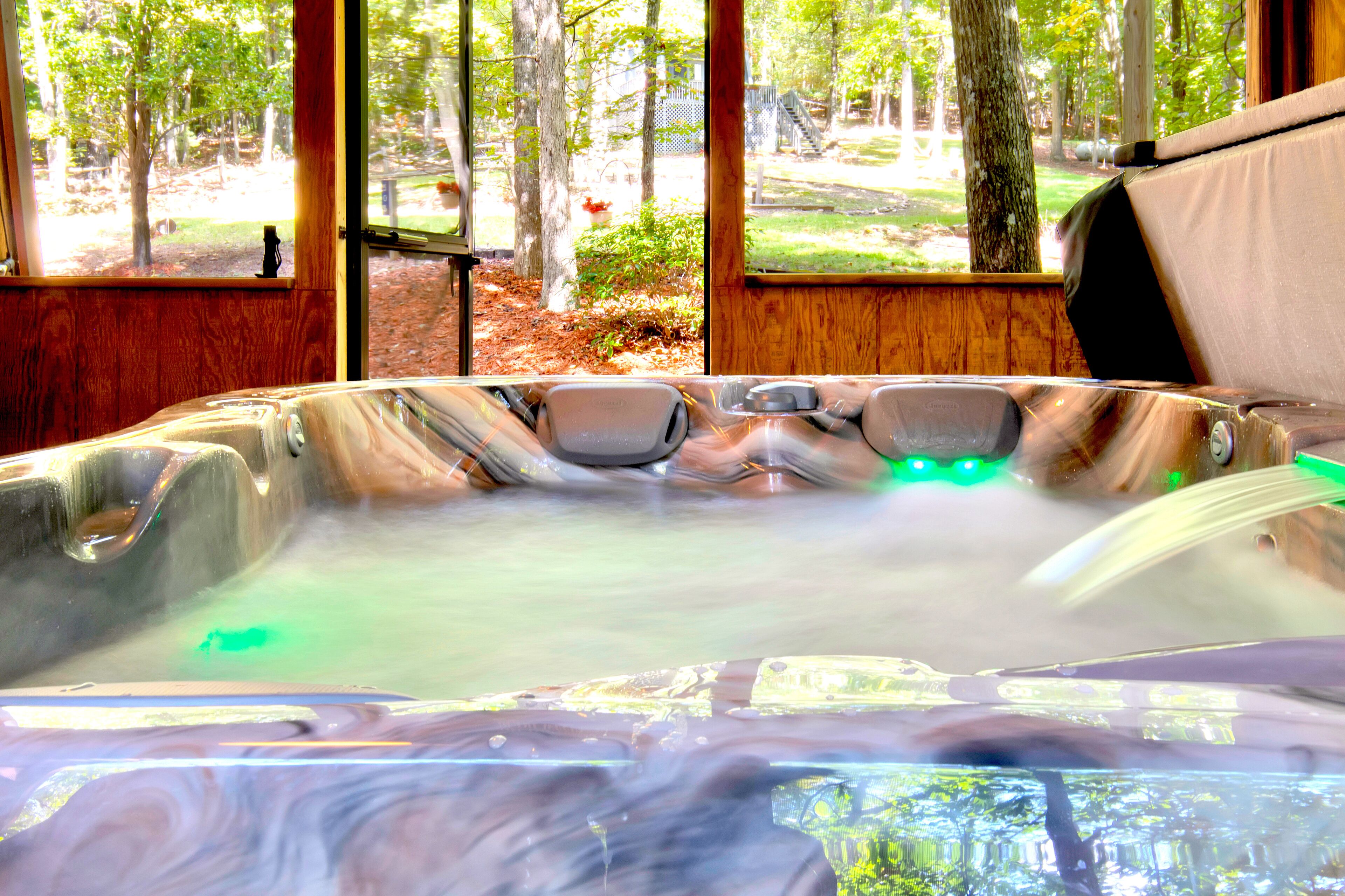 A hot tub with a view of a forest through large windows.