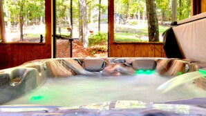 Een jacuzzi met uitzicht op een bos door grote ramen.