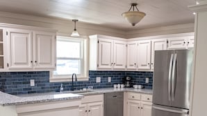 Una cocina con armarios blancos, un refrigerador de acero inoxidable y un salpicadero de azulejos azules.