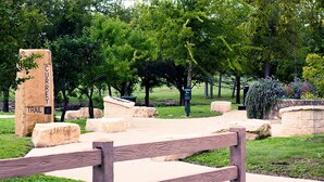 Un parque con un banco de madera, un cartel de piedra que dice 'CURREY TRAIL' y un indicador verde.