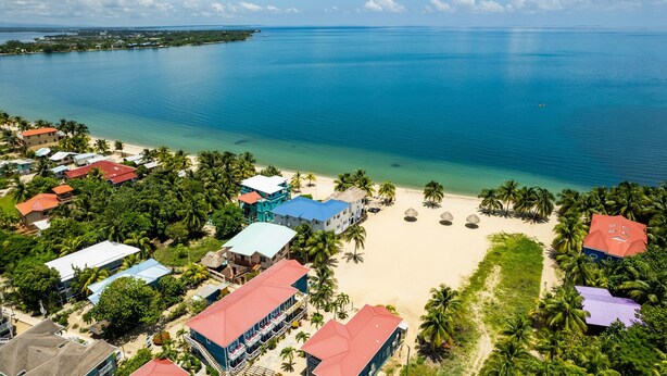 Vista aérea de una zona costera con playa, agua azul cristalina y varios edificios con tejados de colores.