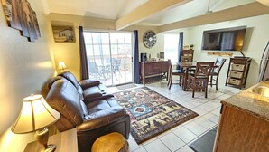 A living room with a leather sofa, a patterned rug, a dining area with wooden furniture, and a kitchen with a TV mounted above the counter. - Bear Mountain Branson Suite Overlooking Pointe Royale Golf Course in Branson! (Branson)