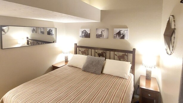 A bedroom with a large bed, a nightstand with a lamp, a mirror, and wall-mounted artwork. - Bear Mountain Branson Suite Overlooking Pointe Royale Golf Course in Branson! (Branson)