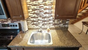 A kitchen with wooden cabinets, a granite countertop, a stainless steel sink, and a backsplash with a mosaic tile design. - Bear Mountain Branson Suite Overlooking Pointe Royale Golf Course in Branson! (Branson)