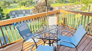 A wooden deck with a table and chairs, an umbrella, and a view of houses and greenery. - Bear Mountain Branson Suite Overlooking Pointe Royale Golf Course in Branson! (Branson)