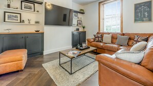 A modern living room with a leather sofa, a coffee table, a flat-screen TV, and a large window.