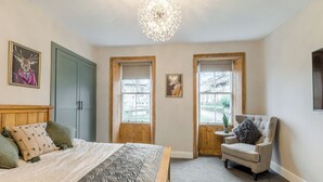 A bedroom with a bed, a chair, two windows, and a chandelier.