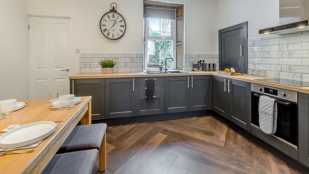 A modern kitchen with dark cabinets, a wooden countertop, a sink, and a clock on the wall.