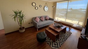 A living room with a grey sofa, a coffee table, a potted plant, and a large window. - Beautiful 2D/2B apartment with pool, barbecue area and AAVV/ (Los Angeles)