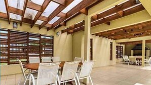 An indoor patio area with a wooden ceiling, white chairs, and a table. - Beautiful 2D/2B apartment with pool, barbecue area and AAVV/ (Los Angeles)