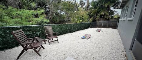 Eine Terrasse mit zwei Holzstühlen, einem kleinen Tisch und einem Gesellschaftsspiel auf einem Kiesbelag.