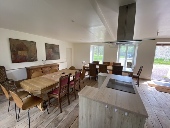 A spacious dining area with a wooden table and chairs, a built-in island with a sink, and two large windows offering a view of the outdoors.