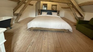 Un dormitorio con techo de madera, una cama, una silla verde y un aparador blanco.