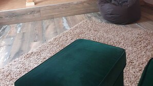Un dormitorio tipo loft con techo inclinado, una escalera de madera, un sillón de cuero color verde y una cama pequeña con almohada verde y naranja.