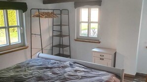 Un dormitorio con cama, ventana, cómoda y estantería metálica.