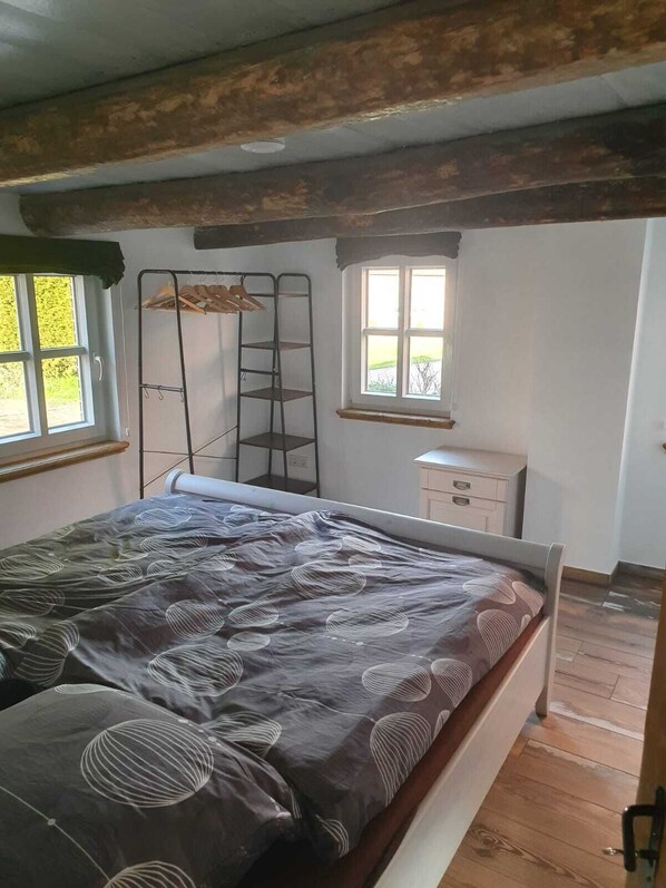 Quarto com cama, janela, cómoda e estante de metal.