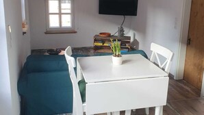 Cocina compacta con una mesa blanca, sillas, una lámpara colgante, una ventana y techo de madera.