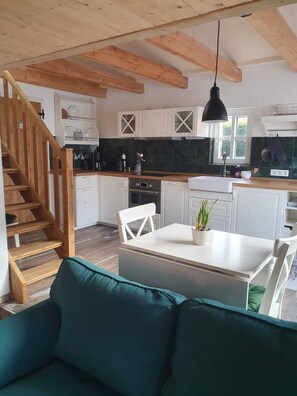 Uma cozinha moderna com armários brancos, escada de madeira e área de jantar com sofá verde.