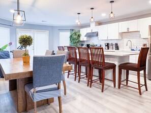 Una cocina moderna con armarios blancos, sillas de madera e iluminación colgante.