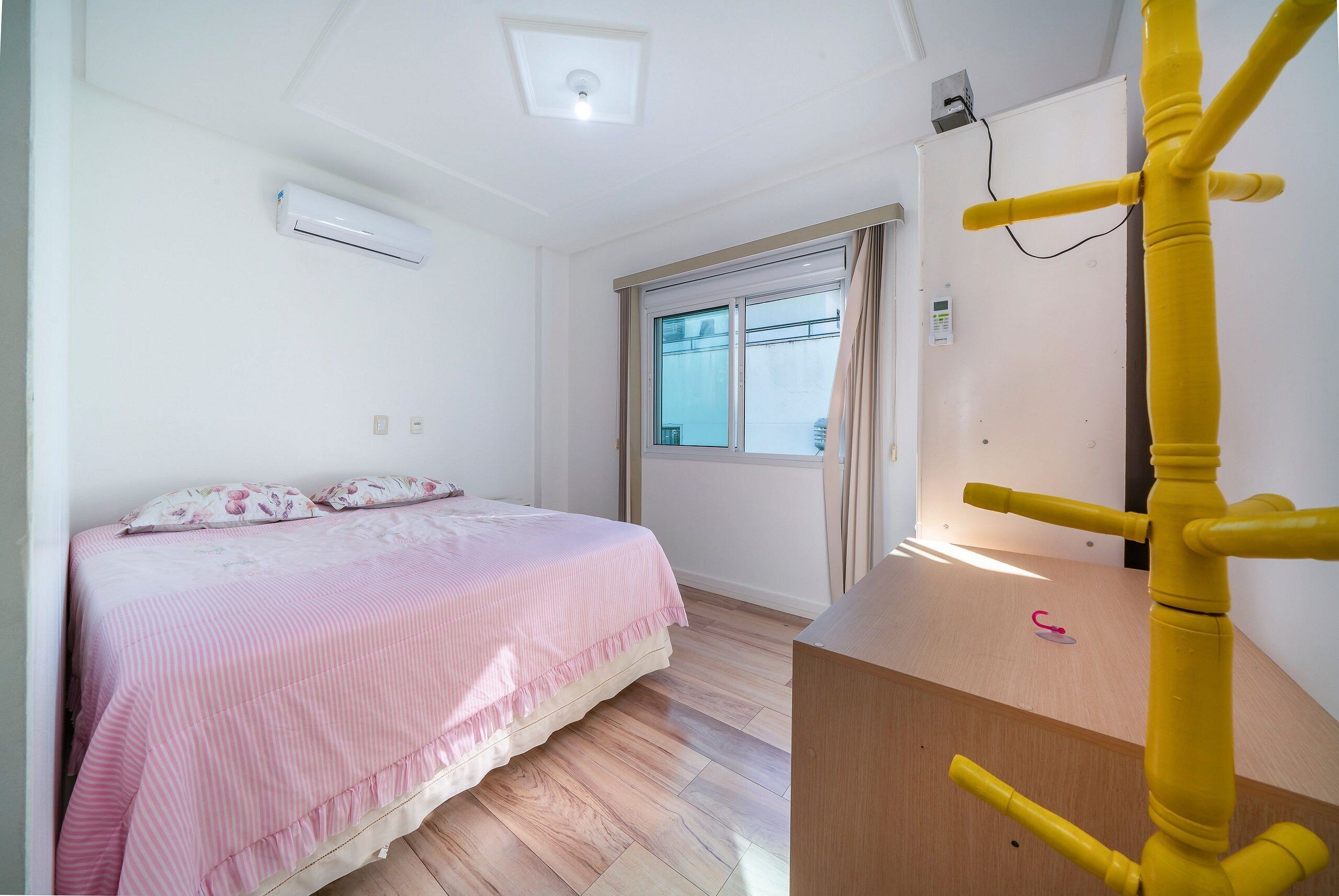 Ein Schlafzimmer mit einem Bett, einem Fenster, einem Nachttisch und einer Wand-Klimaanlage.