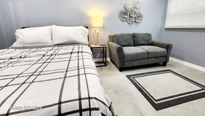 Una camera da letto con un letto, un divano grigio, un comodino con una lampada e un elemento decorativo a parete.