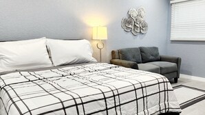 Una camera da letto con un letto, un divano grigio, una lampada a parete e un elemento decorativo a parete.