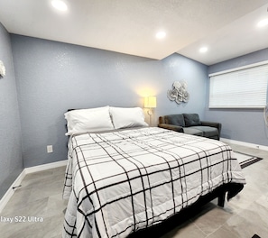 A bedroom with a bed, a sofa, a wall-mounted lamp, and a decorative wall piece. - Studio 3 ! (Lakeland)