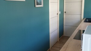 Ett kök med turkosa väggar, träskåp och en vit bänkskiva. På väggen hänger två inramade tavlor och det finns en vit dörr.