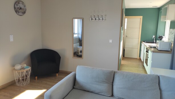 Ett vardagsrum med en grå soffa, en svart fåtölj, en rund träklocka, ett litet sidobord med en dekorativ prydnad och en spegel på väggen.